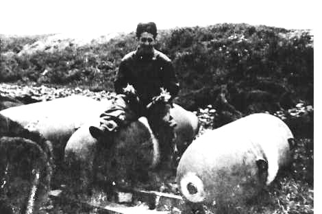 PFC Adolph Cello, 526th Squadron Ordnance Detachment, sitting on a 1,000lb bomb holding two tail fuses